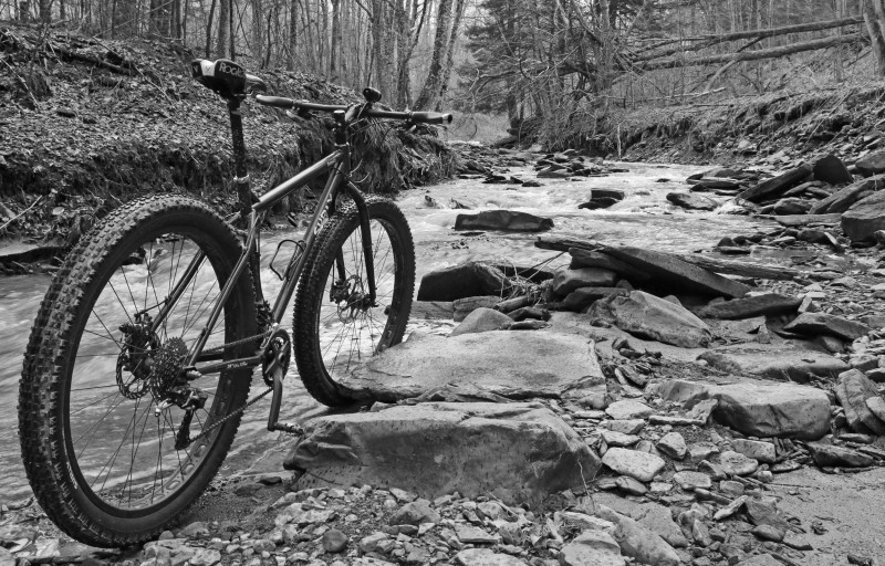 Rear view of a Surly bike, standing in rocky stream, in a forest - black and white image