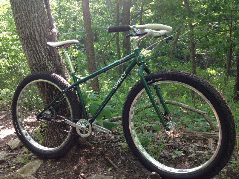Right side view of a Surly Krampus bike, parked against a tree, in a green forest