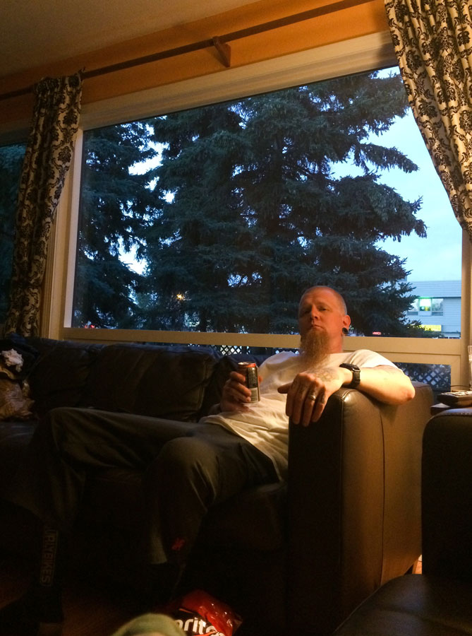 Front view of a person, sitting on a couch, in a room with a window showing the trees on the outside