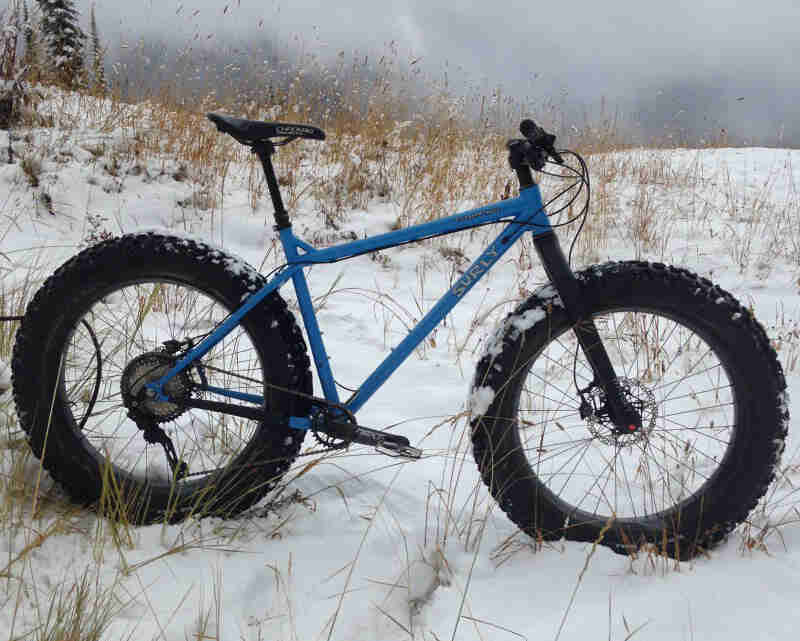 Right side profile of a Surly fat bike, blue, parked in a snow covered field