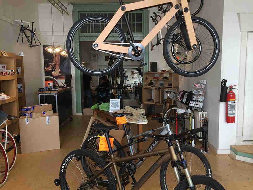 Right side view of a wood framed bike, hanging from a ceiling in a bike shop