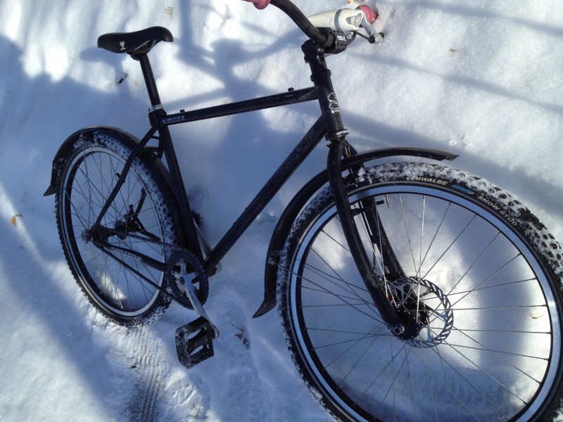 Right side view of a black Surly 1x1 bike with fenders, leaning against a tall snow bank