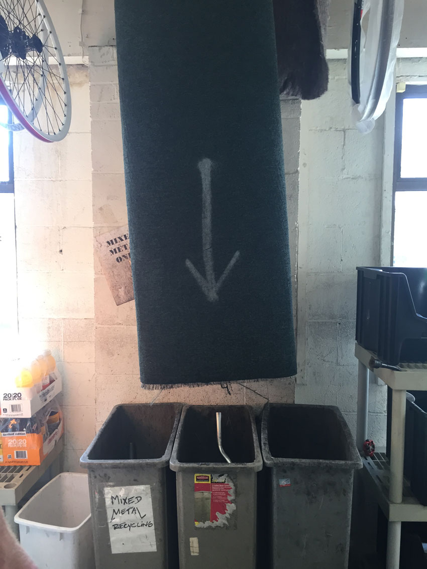 A chute hanging above 3 plastic bins, in a room