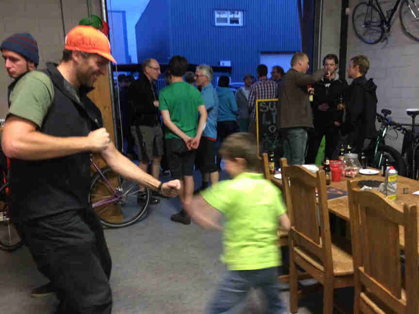 Side view of an adult, play boxing with a child, in a garage with people standing around