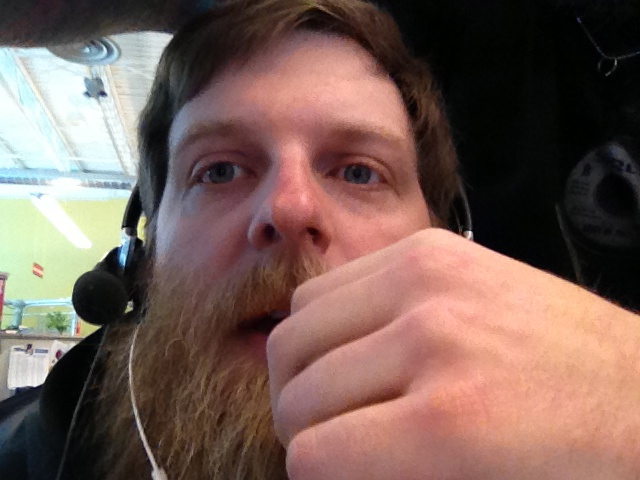 Headshot of a person with a beard, wearing a headset, with a hand in front of their mouth