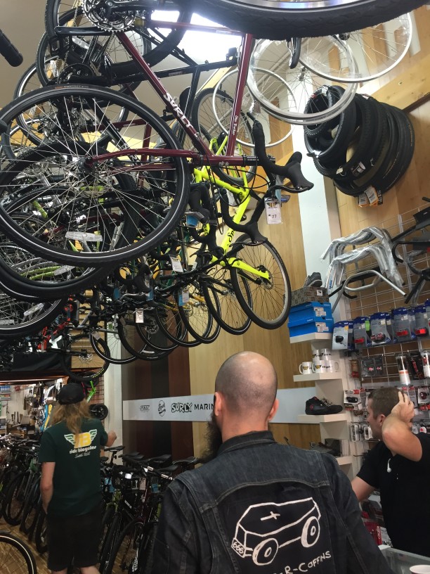Rear view of people in a bike shop, with a row of bikes hanging on racks, above them