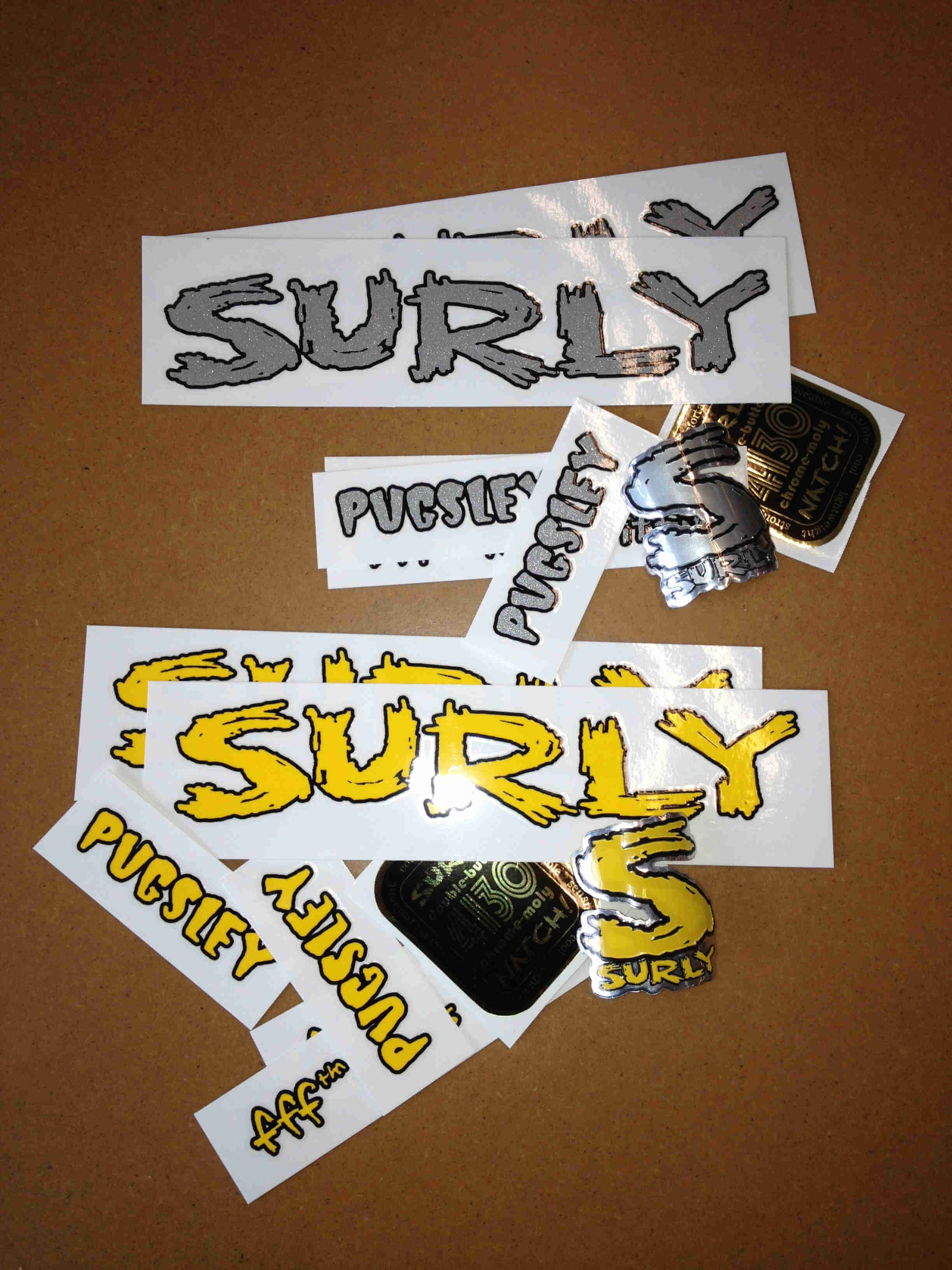 Downward view of Surly Pugsley bike decals, laying scattered on a brown surface