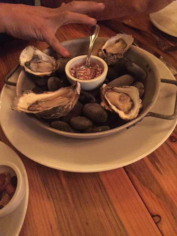 A hand above a pan of oysters in a half shell, on a wood table top