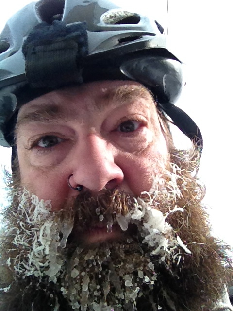 Headshot of a cyclist wearing a bike helmet, with an icy beard and mustache