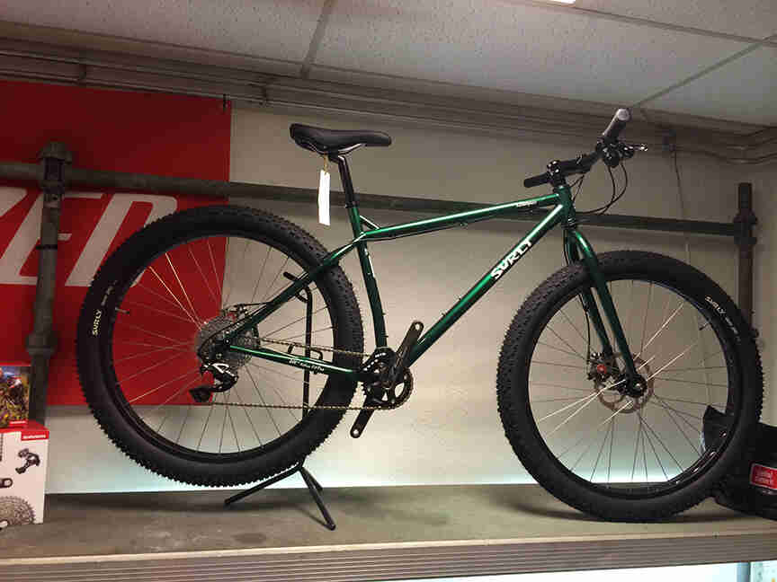 Right side view of a green Surly Krampus bike, standing up on a shelf, in a room with white walls
