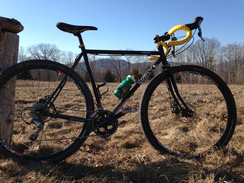 Right side view of a black Surly Straggler bike, parked against a post, with a field of brown grass behind