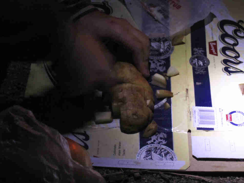 A hand cutting up a potato on a flattened Coors beer box