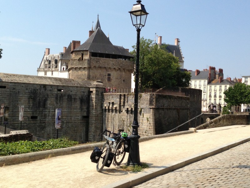 Front left side view of a Surly bike with gear, leaning against a light pole on a gravel trail, with a castle behind it