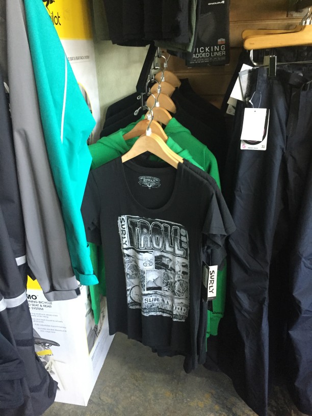 A retail rack of clothes mounted to a wall, with a black Surly Troll shirt in front view