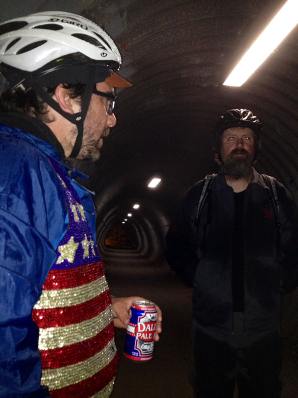 Two people, wearing cyclist attire, standing in a concrete tunnel with lighting above