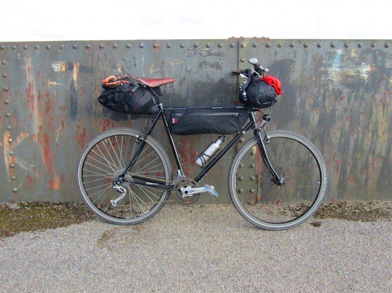 Right side view of a black Surly bike with gear packs, leaning against a steel wall with rivets