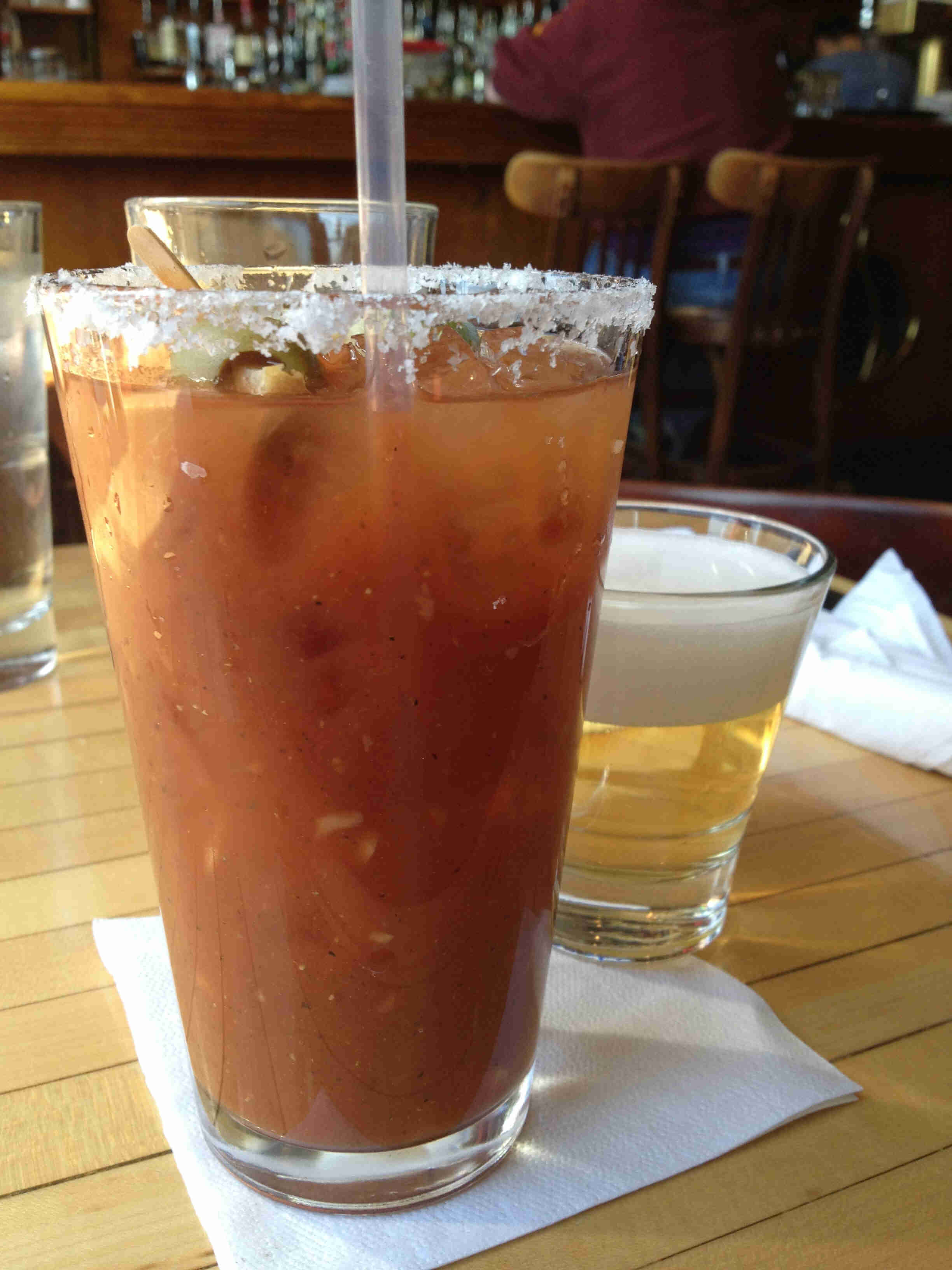 Close up view of a bloody mary drink in a glass, next to a beer chaser, on a table inside a bar
