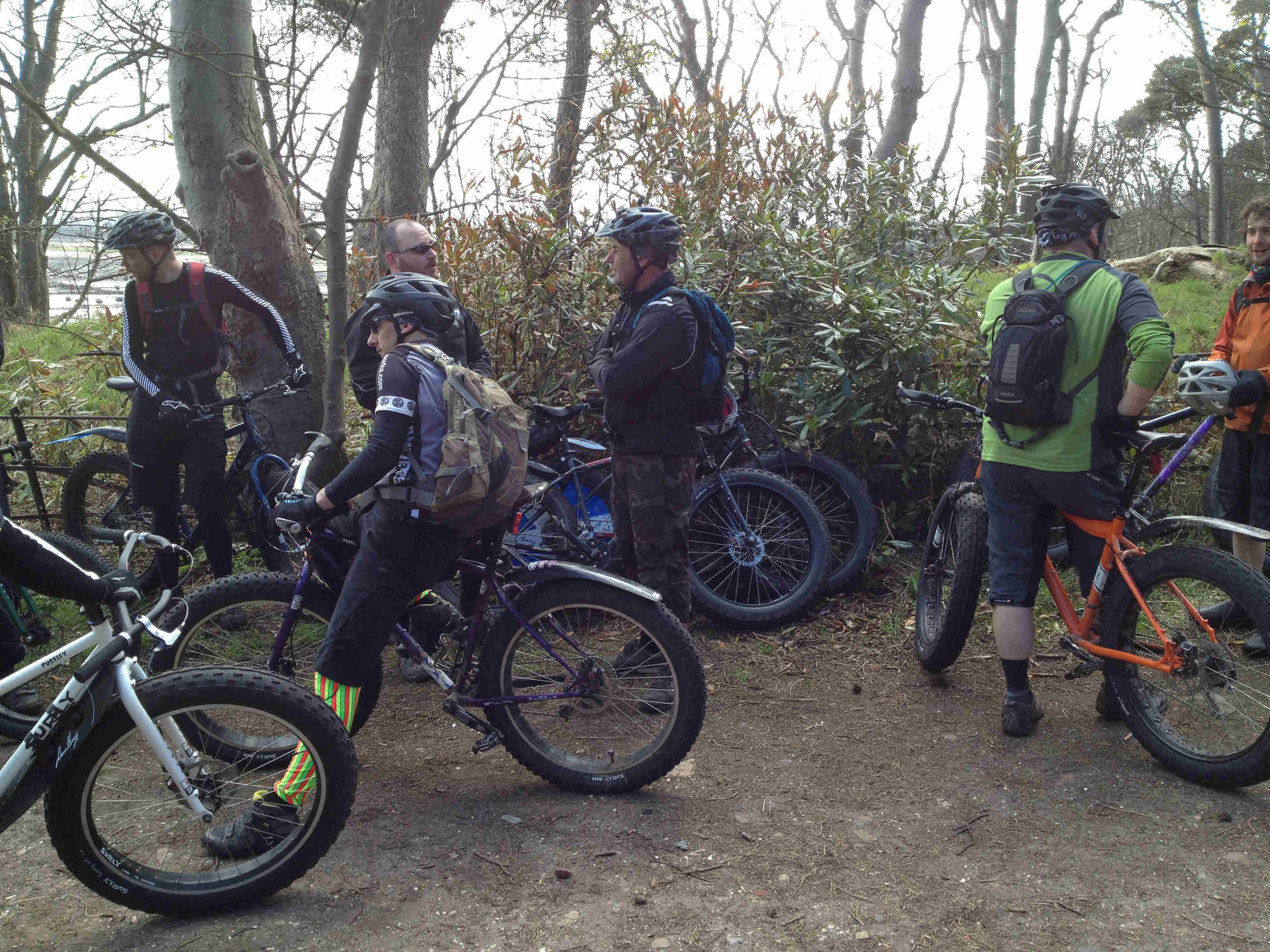 A group of cyclists, standing around with their Surly fat bikes, on a dirt clearing in the woods