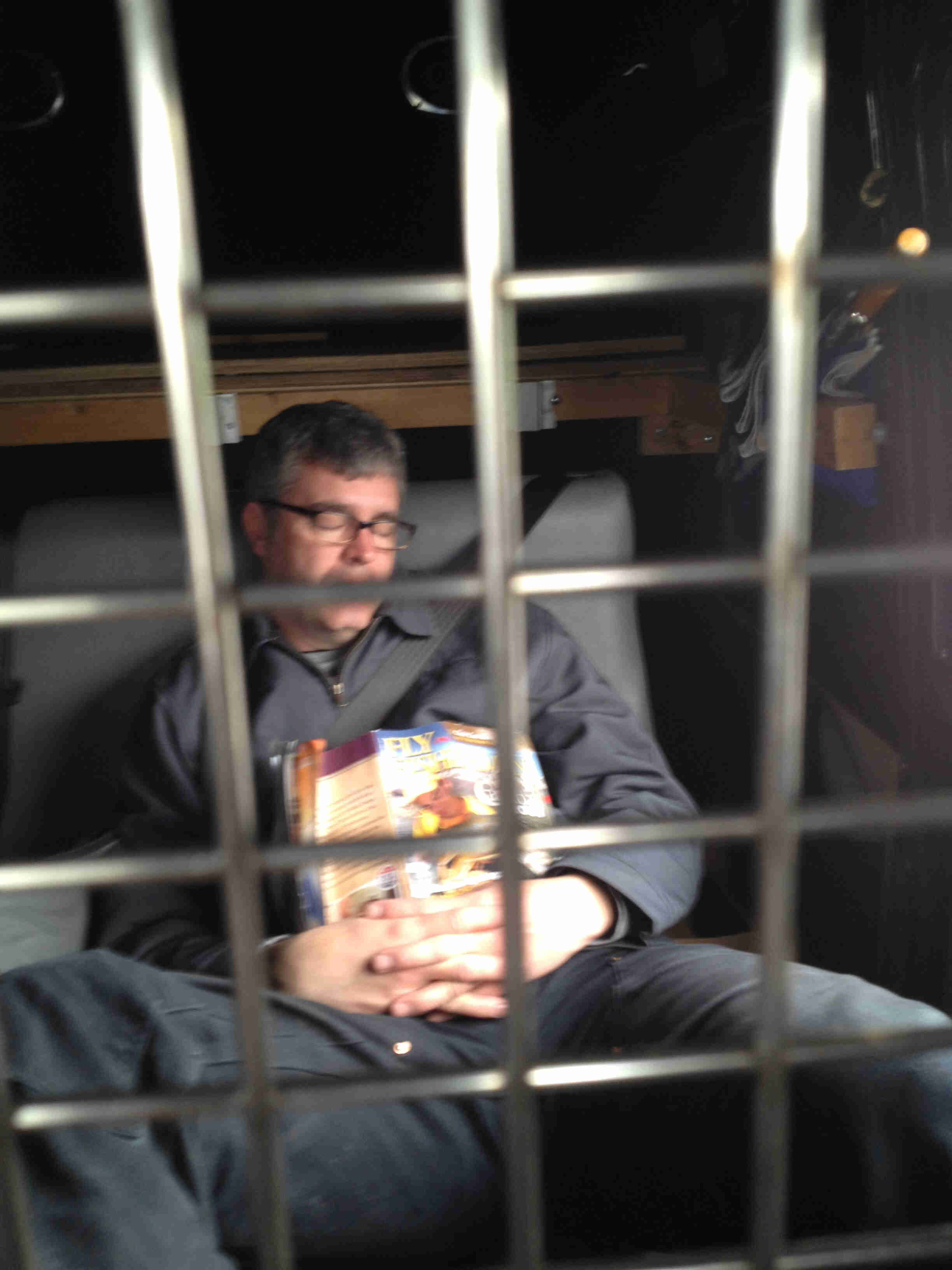 Front view of a person sleeping with a book on their chest, behind a grid of steel bars
