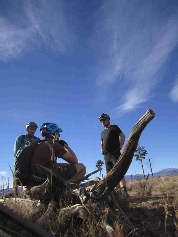 Upward view of 3 cyclists, in a brown, grassy field
