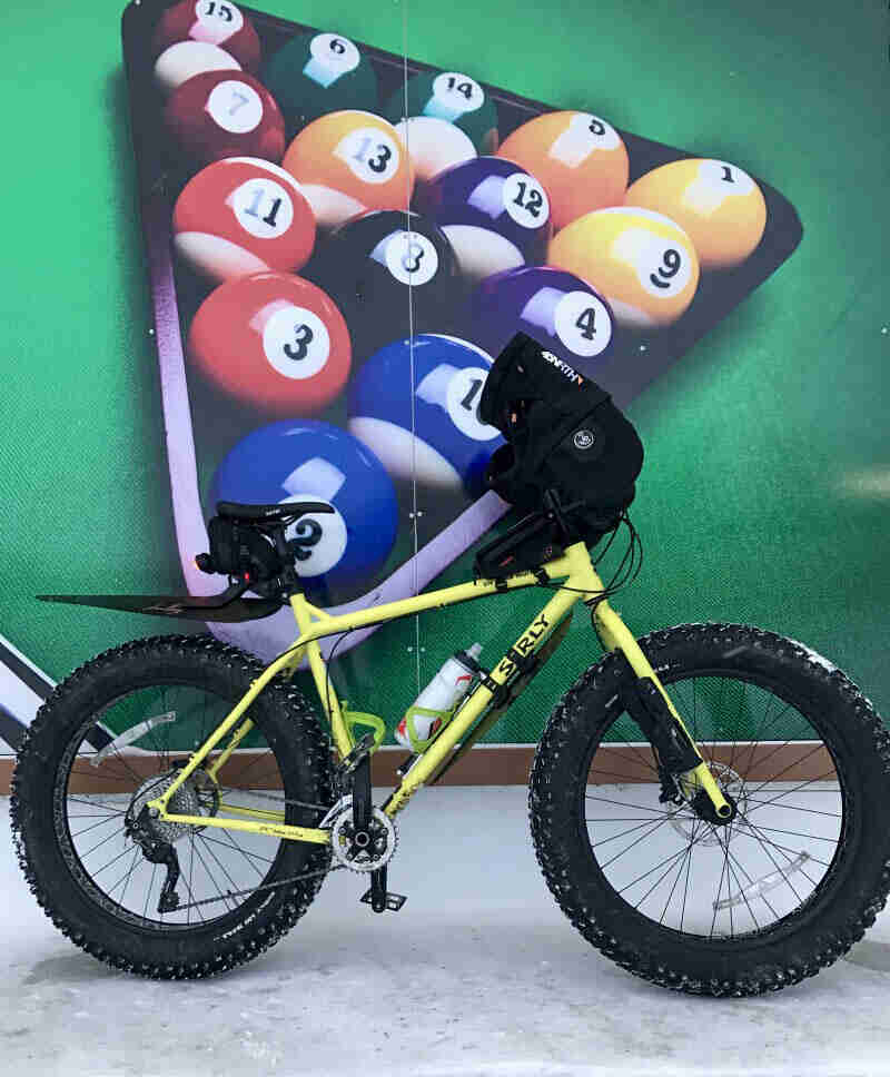 Right side view of a yellow Surly fat bike in front of a wall with a mural of pool balls in a rack