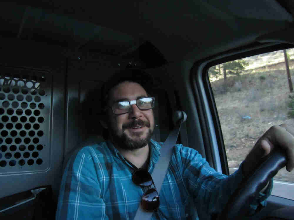 Front view of a person wearing glasses with tape on the bridge, behind the steering wheel of a motor vehicle