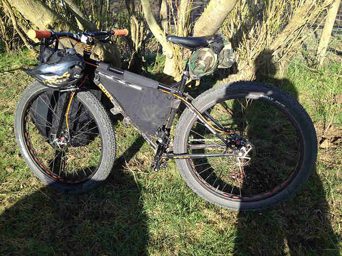 Left side view of a black Surly Pugsley fat bike with a frame pack, parked on grass next to a cluster of small trees