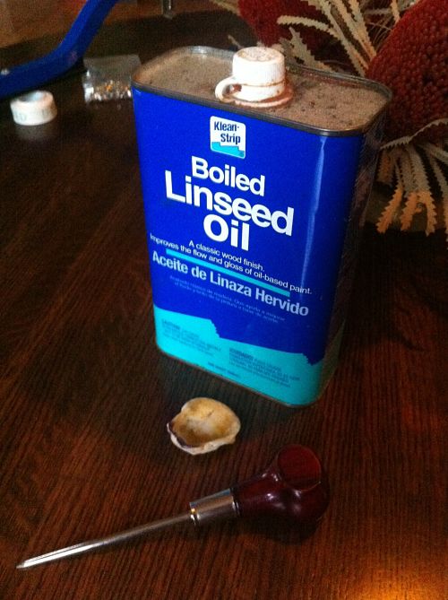 A can of boiled linseed oil and a scratch awl tool, sitting on a wood table with other various items