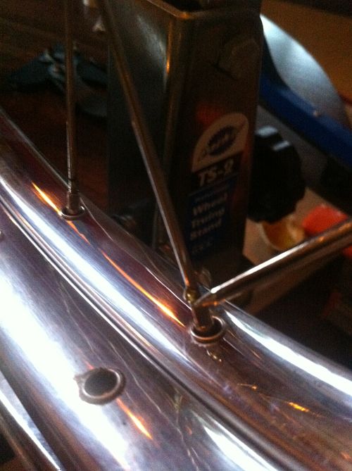 Close up view of the end of a scratch awl tool, applying linseed oil to the threads of a bike spoke, mounted to a rim