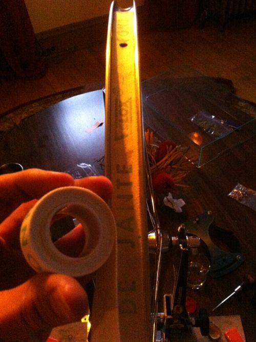 Straight on, downward view of a bike rim, with a person's fingers holding rim tape, on a wood table in a dimly lit room