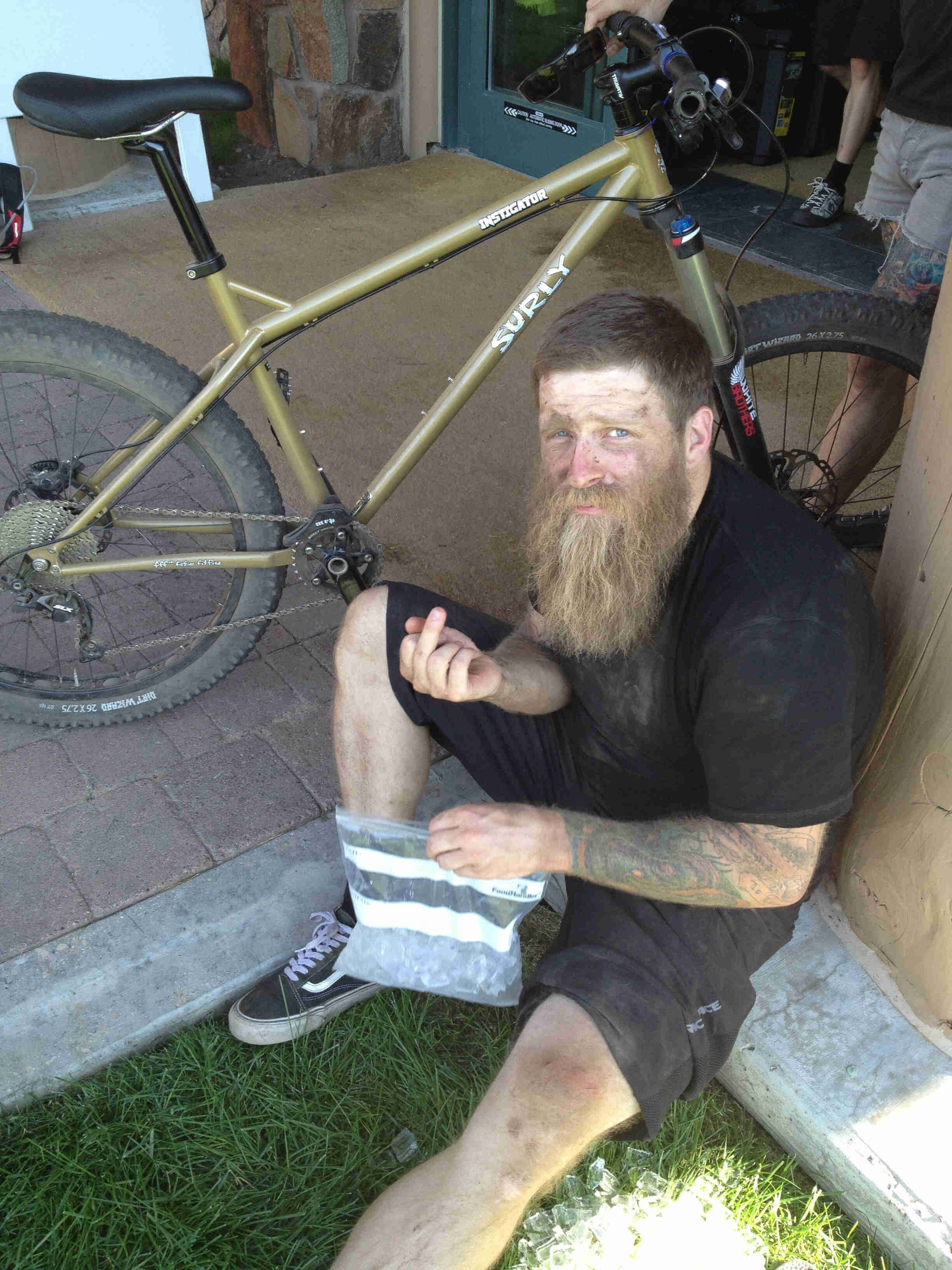 Downward view of a person, sitting in front of a Surly Instigator bike, icing their knee and showing their middle finger