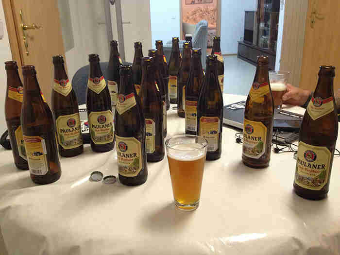 A table inside of a room, with a glass of beer and many Paulaner bottle sitting on top