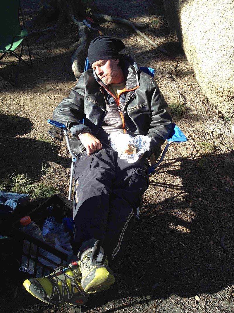Downward, front view of a person sleeping in a camp chair, food on foil sitting in their lap
