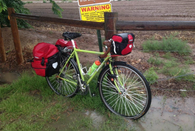 Right side view of a lime green Surly bike with gear packs, parked next to a fence with a farm field in the background