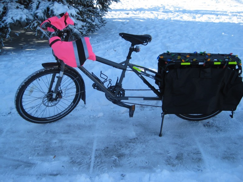 Left side view of a gray Surly Big Dummy bike, with pink hand warmers, parked on a snowy sidewalk