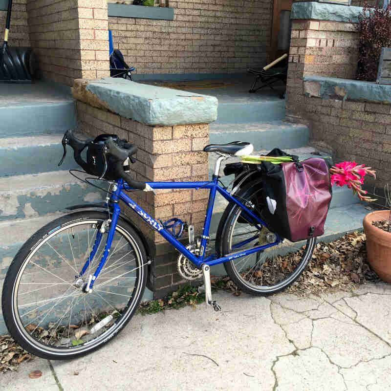 Left side view of a blue Surly bike, parked against a brick column between 2 stairways