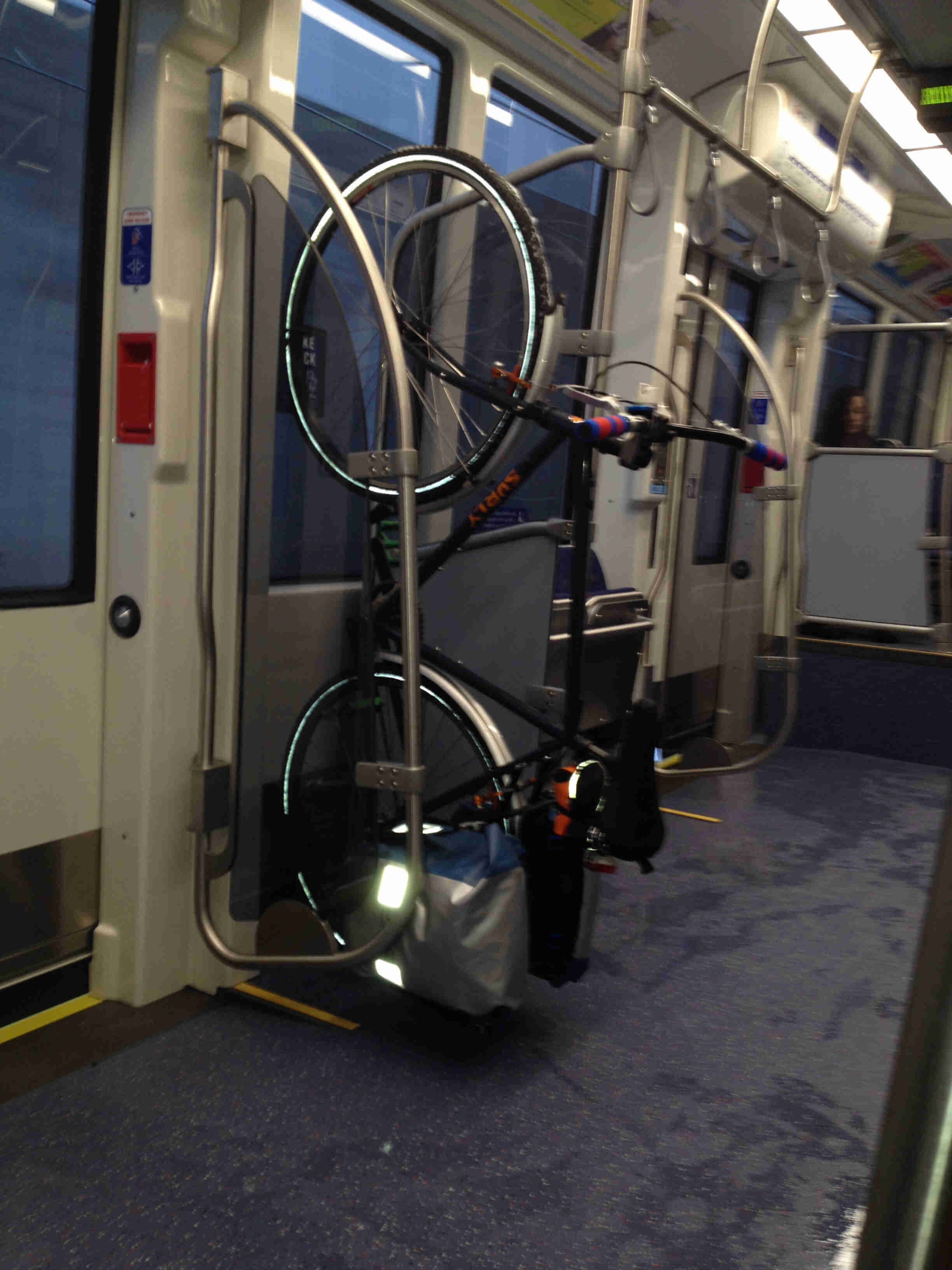 Left side of a black Surly bike with fenders, standing up vertically, inside of a city rail car