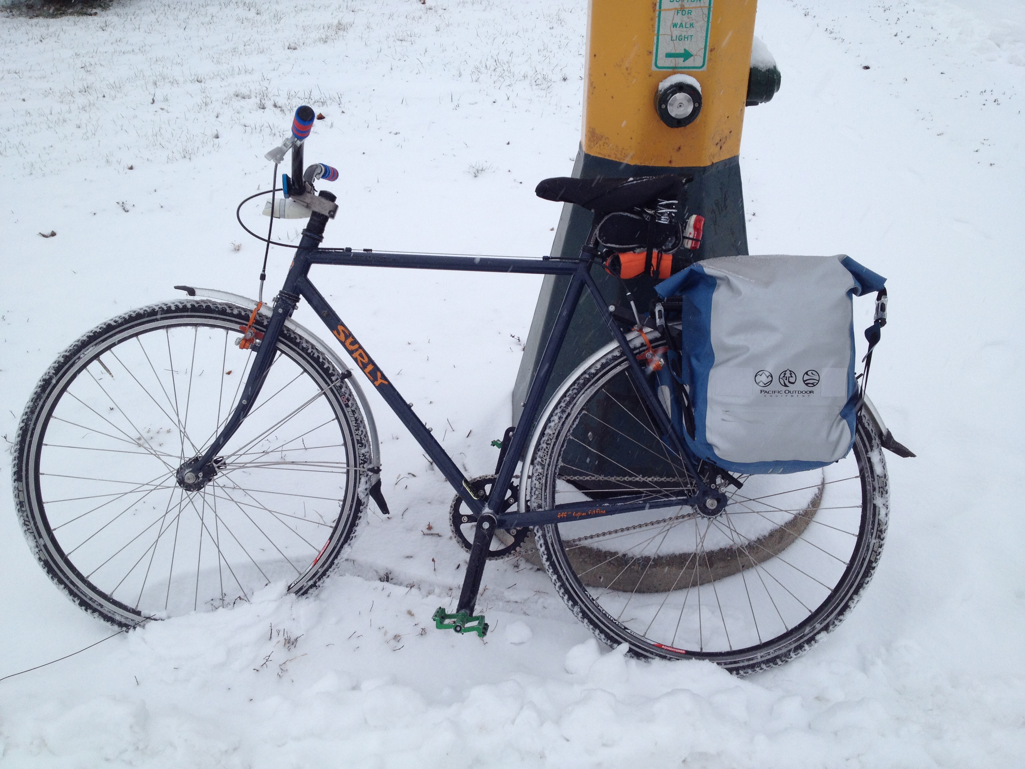 Left side view of a Surly bike, standing in snow, leaning against the base of a traffic light pole