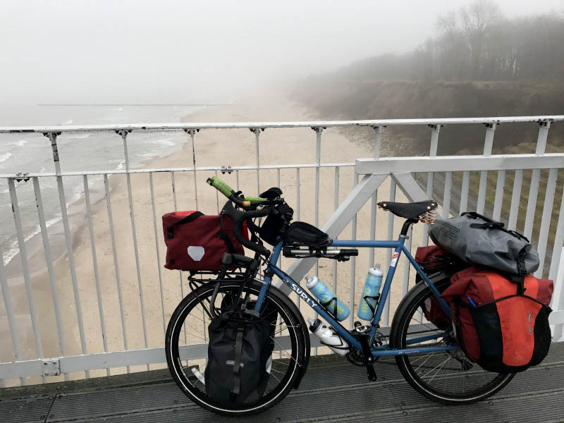 Left side view of a Surly bike, loaded with gear, on a bridge over a seashore, with fog in the background