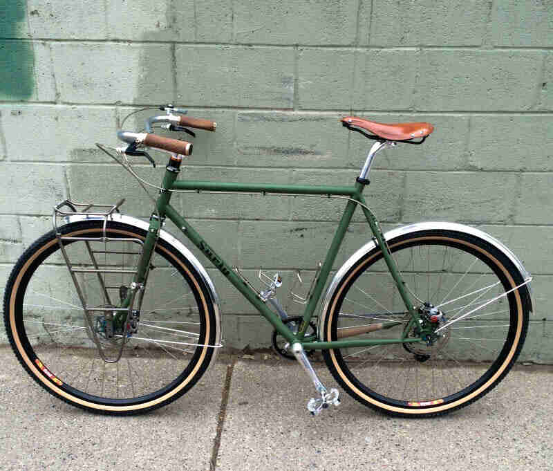 Left side view of a green Surly bike, parked on a sidewalk, along a cinder block wall