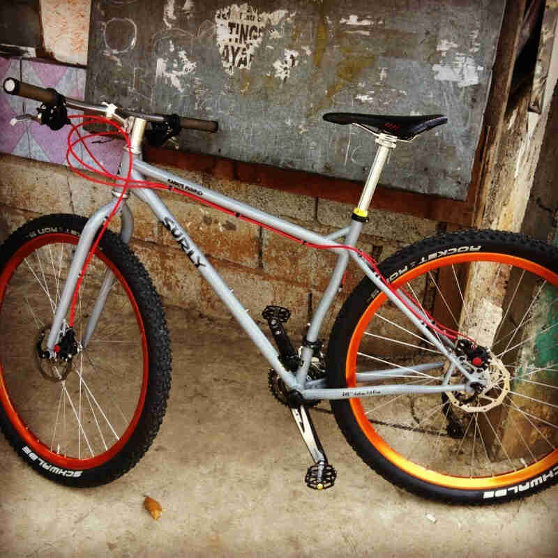 Left side view of a gray Surly Karate Monkey bike, with copper rims, leaning against a cinder block wall