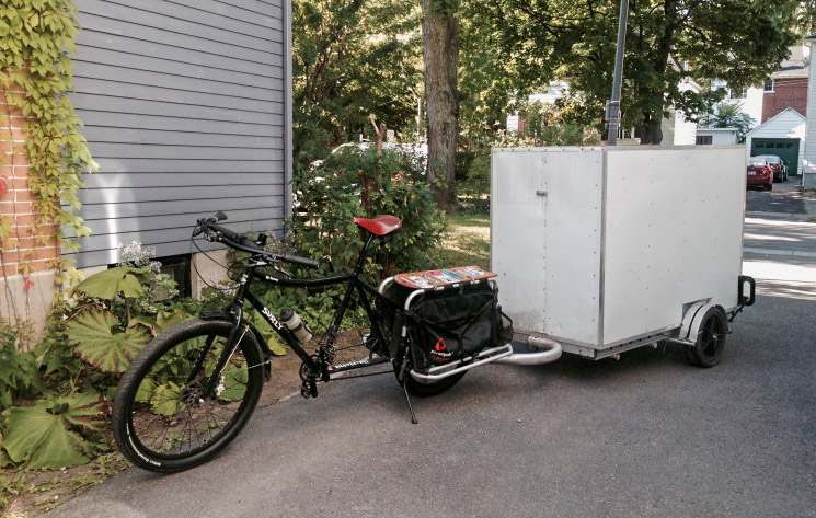 Left side view of a Surly Big Dummy big with a trailer behind, on a driveway, next to a gray house