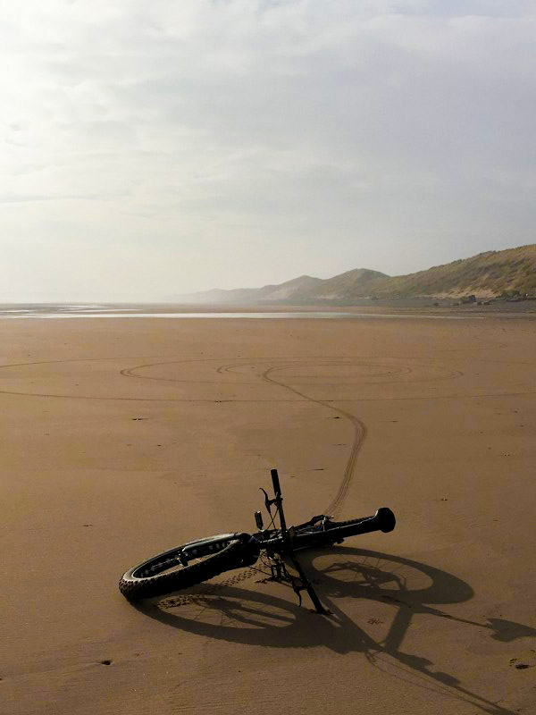 Front view of a Surly bike laying on it's side in sand, with a large, flat, sandy area in the background