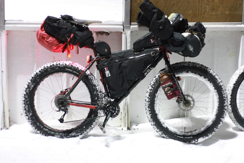 Right profile of a Surly fat bike loaded with gear, in front of a white wall
