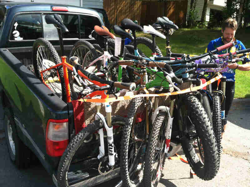 Rear view of a truck bed, loaded with Surly bikes, in a driveway with a person standing near