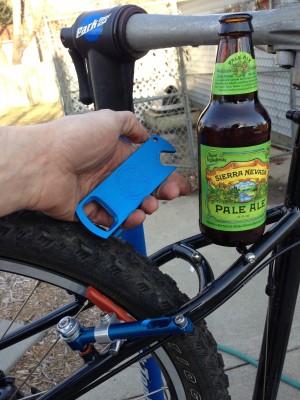 Rear, right side view of a hand holding an opener, next to a beer bottle that's on the seatstay of a Surly Troll bike
