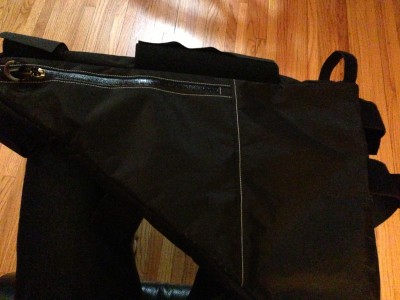Downward, right side view of a black Surly frame bag, laying on a wood floor