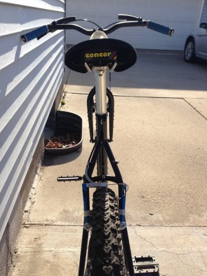 Rear view of a Surly Troll bike, leaning against the side of a house, facing a garage on a driveway