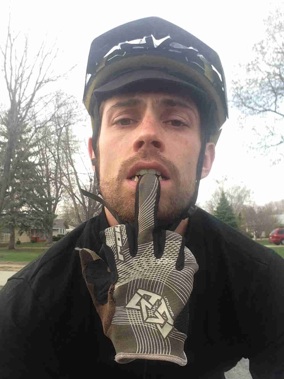 Headshot of a person, wearing a bike helmet, biting the middle finger of a glove
