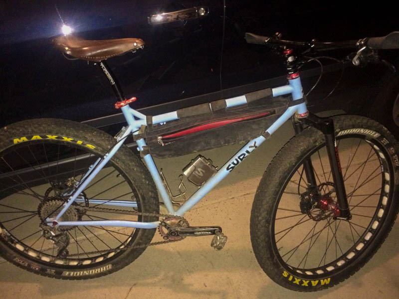 Right side view of a light blue Surly fat bike on a sidewalk at night